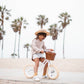 Child riding a bike with a basket on a beach with palm trees in the background