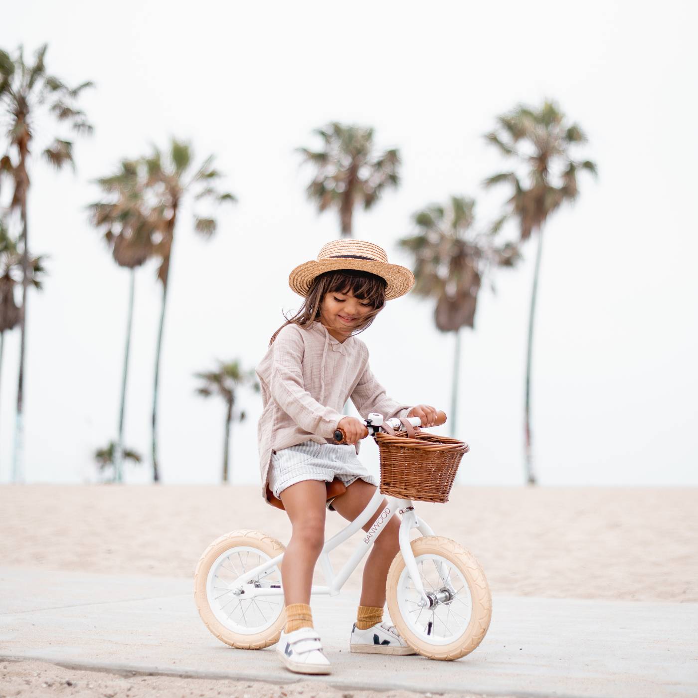 Child riding a bike with a basket on a beach with palm trees in the background