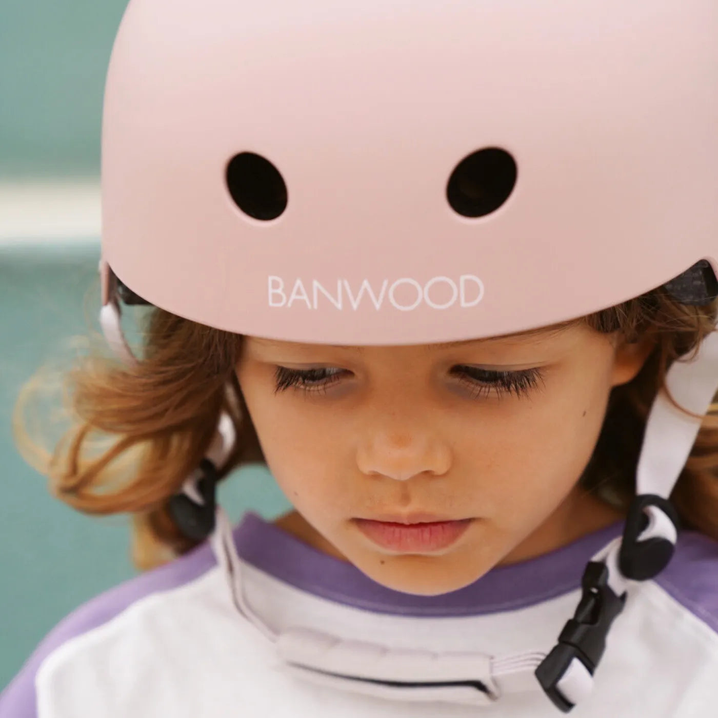 Child wearing a pink helmet with 'Banwood' branding against a blurred background