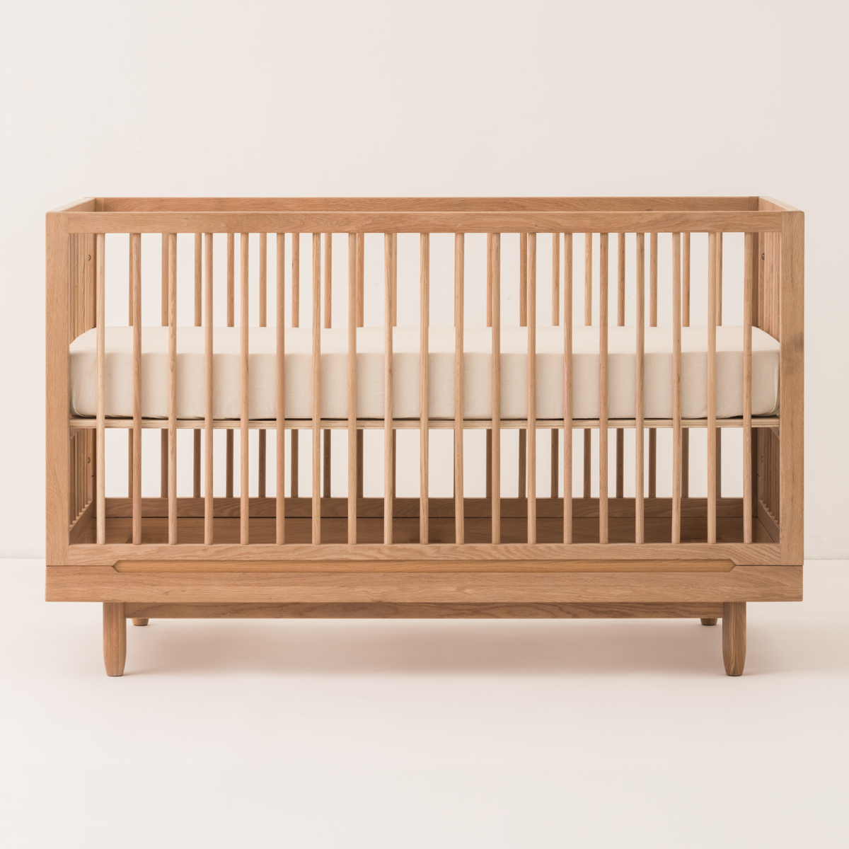Wooden crib with white mattress on a beige background