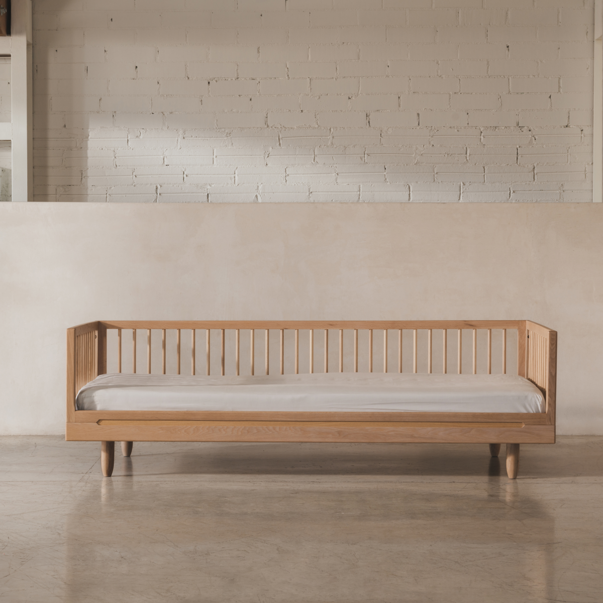 Wooden bed with a gray mattress in a minimalistic room with a brick wall.