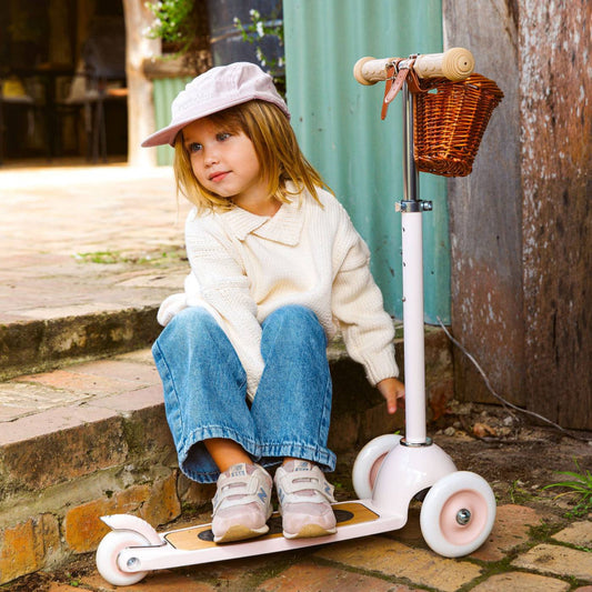 Child sitting on a scooter with a basket in an outdoor setting