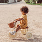 Child riding a tricycle with a basket on a gravel path.